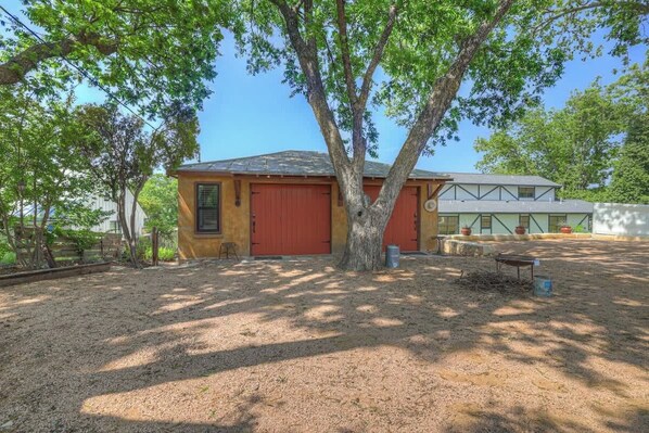 A house with a red garage door, a large tree in front, and a gravel driveway.