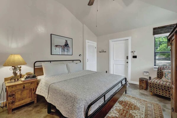 A bedroom with a bed, bedside table, lamp, and a chair.