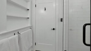 Un baño con paredes de azulejos blancos, una puerta blanca y una cabina de ducha de vidrio.