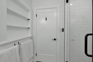 A bathroom with white tiled walls, a white door, and a glass shower enclosure.