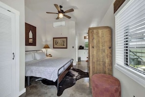Un dormitorio con cama, ventilador de techo, armario de madera y ventana con persianas.