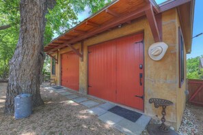 A rustic building with two red garage doors, a wooden porch, and a metal bench. - Casa Salvia Tejas Suite Walking Distance to MainSt! (Fredericksburg)