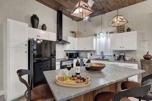 Een moderne keuken met witte kastjes, een roestvrijstalen koelkast, een houten kookeiland met een fruitschaal en wijnglazen, en hanglampen.