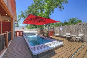 A hot tub on a wooden deck with a red umbrella, surrounded by a wooden fence and outdoor furniture.
