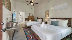 A hotel room with two beds, a ceiling fan, a wooden headboard, a small table with a decorative item, and a colorful rug.