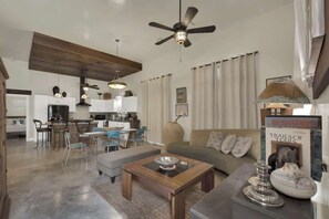 A spacious living area with a modern kitchen in the background, a ceiling fan, and a dining area with chairs and a table.