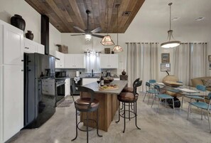 A modern kitchen with white cabinets, a black refrigerator, and a wooden island with bar stools.