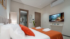 Une chambre d’hôtel moderne, dotée d’un grand lit, d’une télévision et d’une salle de bain visible à travers une porte ouverte.