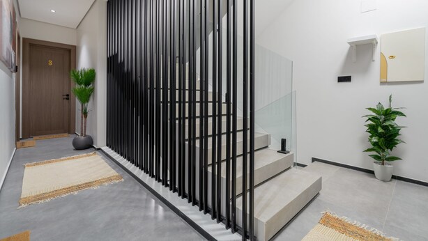 Un couloir moderne avec une porte en bois portant le numéro « 3 », un séparateur vertical noir et un escalier doté de rampes en verre.
