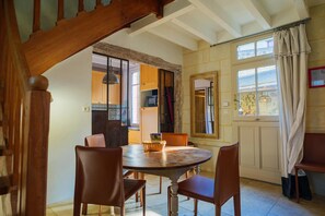 Un coin repas avec une table ronde en bois et quatre chaises, un escalier en bois, et une vue sur la cuisine par une porte ouverte.