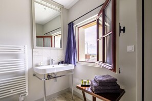 Une petite salle de bain avec un lavabo blanc, un miroir, une fenêtre donnant sur un paysage agréable et un porte-serviettes.