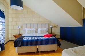 Een slaapkamer met een schuine kap, een bed met een gestreept dekbedovertrek, twee nachtlampjes en een blauwe muur.