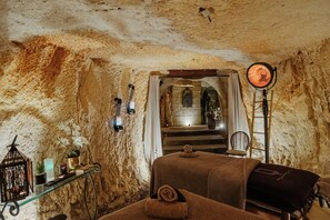 Une salle de spa avec un mur en pierre, une table de massage, une petite table avec des bougies et un radiateur.