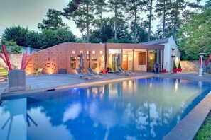 A modern outdoor pool area with a wooden deck, lounge chairs, and a glass-enclosed building. - Les Suites Du Cha Teau (Candes-Saint-Martin)