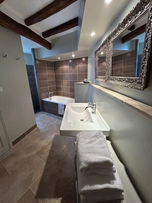 Un baño moderno con bañera, lavamanos y un espejo grande.