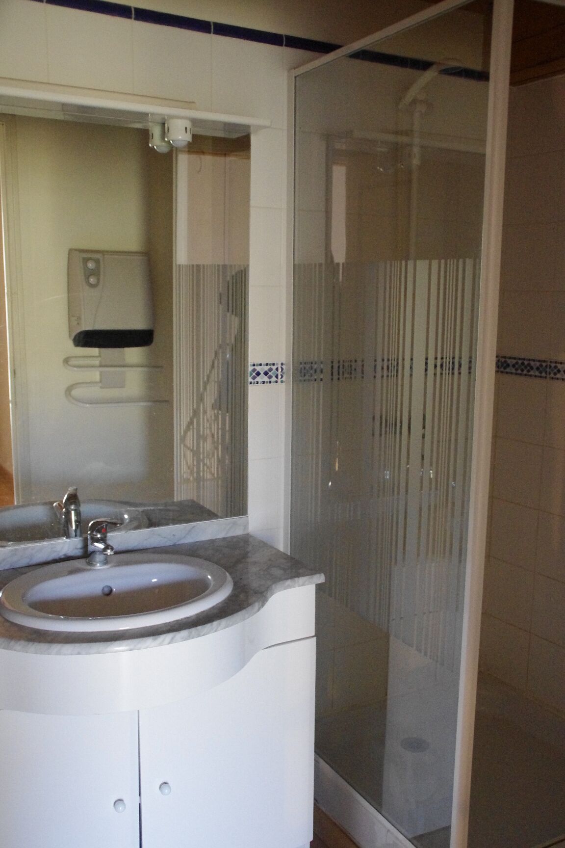 A bathroom with a sink, mirror, and shower enclosure.
