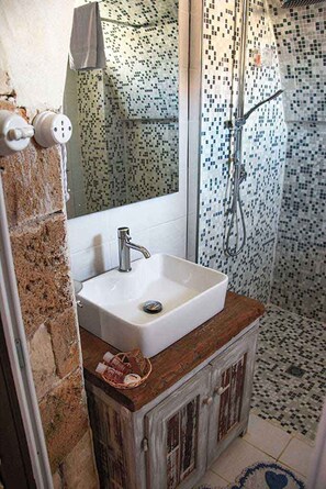 Uma casa de banho com uma pia branca, um armário de madeira e um chuveiro com mosaicos.