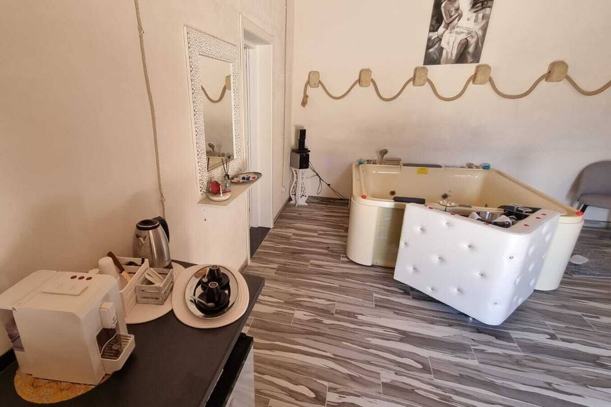 A room with a coffee machine, a sink, and a white tufted ottoman.