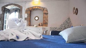 A bedroom with a blue bedspread, a white blanket, a stone archway, a round mirror, and a wall with a mosaic pattern. - Il Casale Rooms&Apartment (Noto)