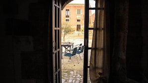 An open doorway leading to an outdoor area with a table and chairs, a building in the background, and a cobblestone path. - Il Casale Rooms&Apartment (Noto)