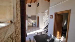 A spacious kitchen with a dining area, wooden beams, and a staircase leading to another level. - Il Casale Rooms&Apartment (Noto)