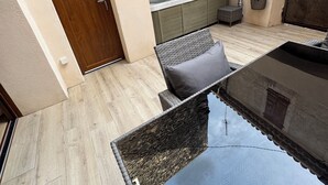 Zona de spa con pared de piedra, puerta de madera, espacio de descanso con una silla y una mesa, y un jacuzzi.