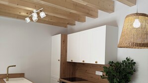 Una cocina moderna con vigas de madera, armarios blancos, encimera de madera y una lámpara colgante.