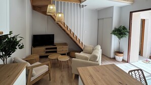 Un interior moderno con una escalera de madera, un sofá, un televisor y un comedor.