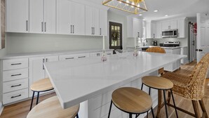 A modern kitchen with white cabinetry, a large island with stools, and a hanging light fixture. - 3BR - Dogs OK! Near the Pointe ~ Hello Sunshine (Emerald Isle)