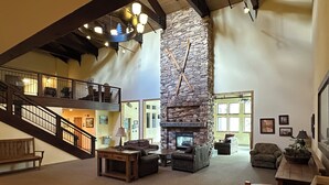 A spacious living area with a stone fireplace, wooden furniture, and a staircase leading to an upper level.