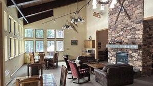 A spacious living area with a stone fireplace, wooden furniture, and large windows providing natural light.
