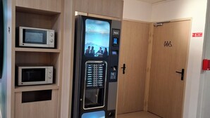 A self-service coffee machine with a digital display, a microwave, and a Nespresso station in a hotel corridor. - Unisotel (Bron)
