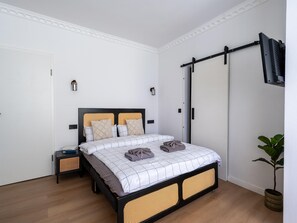 Ein Schlafzimmer mit Bett, Nachttischen, einem an der Wand montierten Fernseher und einem Schiebetürenschrank.