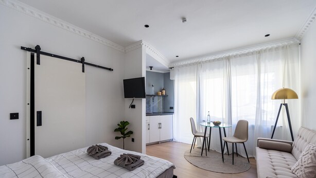 Egy modern szállodai szoba, amelyben található egy ágy, egy kanapé, egy étkezősarok asztallal és székekkel, egy televízió és egy konyhasarok.