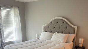 A neatly made bed with a tufted headboard, a bedside table with a lamp, and a window with blinds. - 3-bedroom townhome in tranquil Delmar with WiFi, AC. Relax and unwind (Delmar)