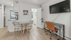 A modern kitchen with white cabinetry, a dining area with a round table and wicker chairs, and a TV mounted on the wall. - Chic City Retreat 93J For 2! (Columbus)