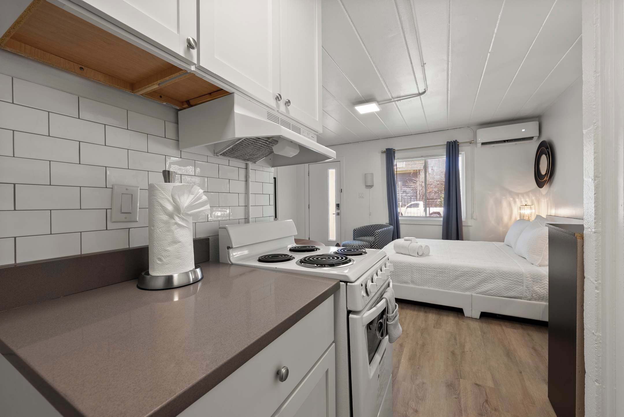 Una kitchenette compacta con estufa, horno y una cama en la habitación contigua.