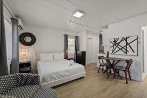 A hotel room with a bed, a desk, a chair, a round mirror, and a painting on the wall.