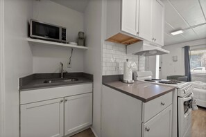A compact kitchen with white cabinets, a microwave, a stove, and a sink.