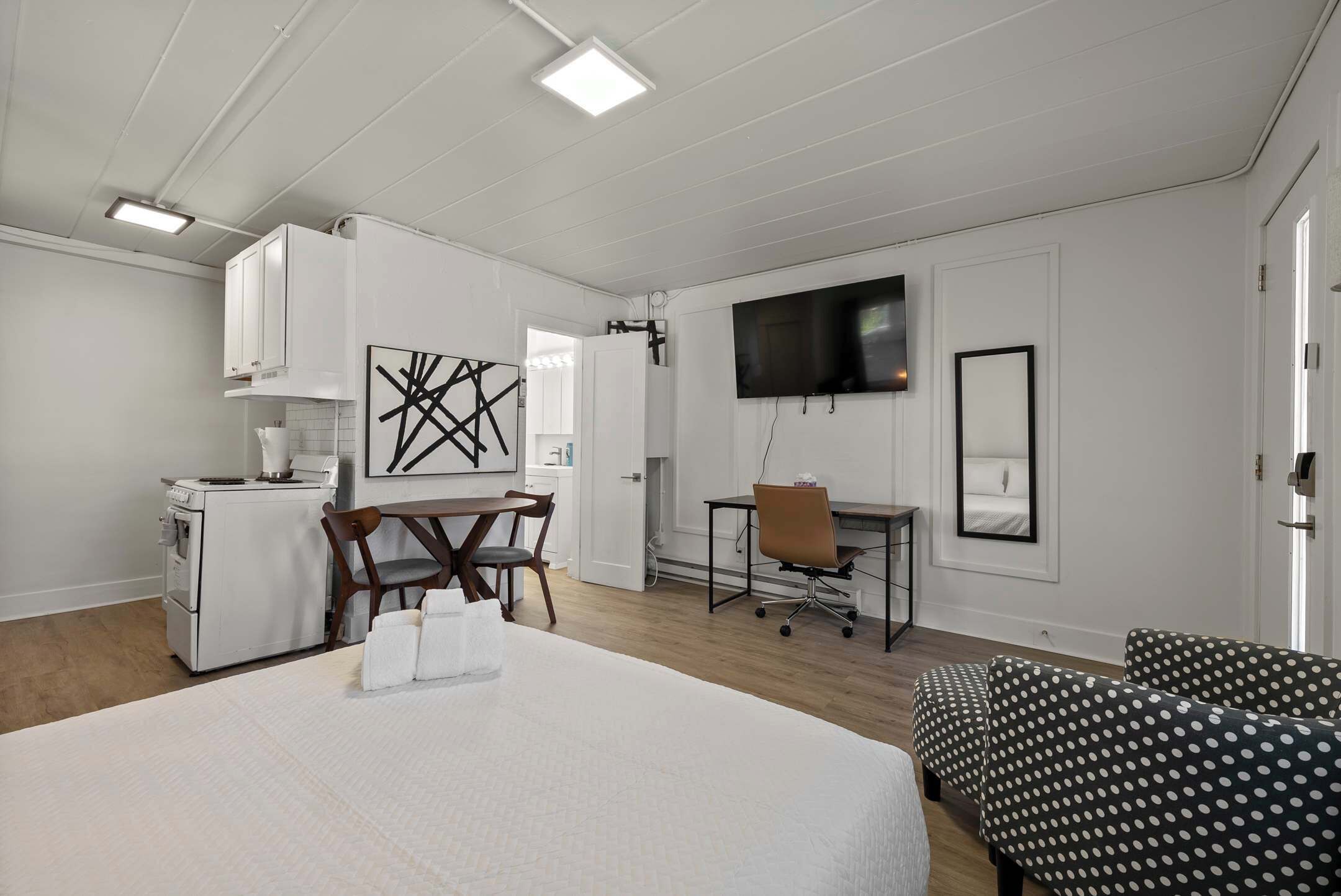 Habitación de hotel con cama, escritorio, silla, televisor y kitchenette.