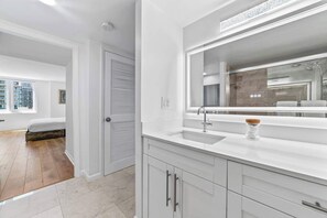 A modern bathroom with a large mirror, white cabinetry, and a visible shower area.