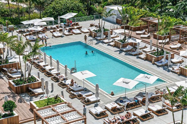 A poolside area with multiple lounge chairs and umbrellas, surrounded by greenery.