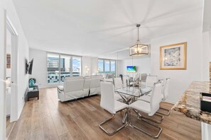 A modern living room with a glass dining table, white sofas, and a city view.