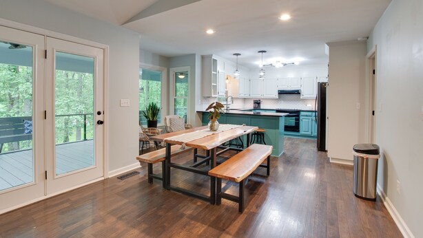 Una cocina amplia con una mesa de madera y bancos, vistas al exterior y un cubo de basura.