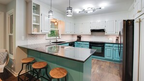Una cocina moderna con armarios blancos, una isla verde azulada con taburetes y electrodomésticos de acero inoxidable.
