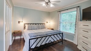Un dormitorio con cama, ventilador de techo, mesita de noche, cómoda y ventana con cortinas.