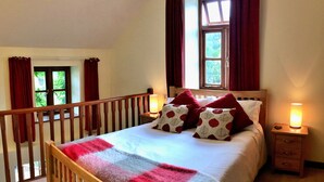 Une chambre avec un lit en bois, deux tables de chevet avec des lampes, une fenêtre avec des rideaux et une vue sur la verdure à l’extérieur.