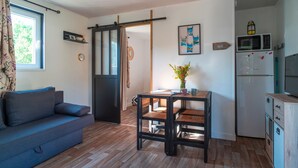 A compact living space with a sofa, a dining table, a kitchen area with a microwave and refrigerator, and a sliding door leading to another room.