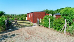 A rural property with a gravel driveway leading to a wooden gate, surrounded by lush greenery and a red building.