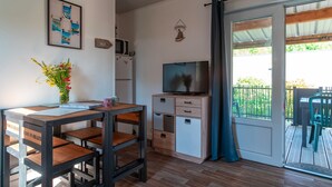 A compact living space with a wooden table, a TV, a small cabinet, and a door leading to an outdoor area with a wooden deck.